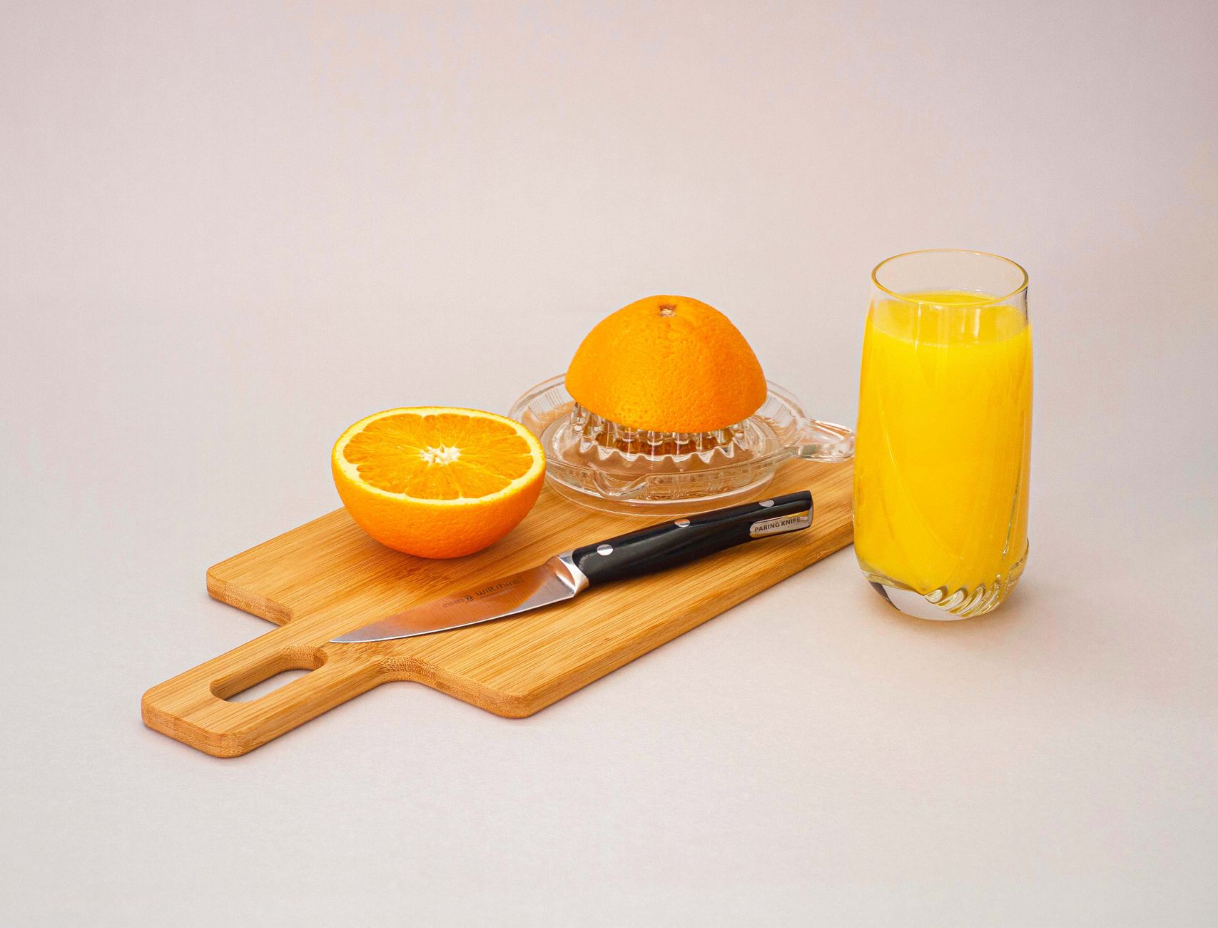 Refreshing setup of fresh orange juice with sliced oranges and a juicer on a wooden board.